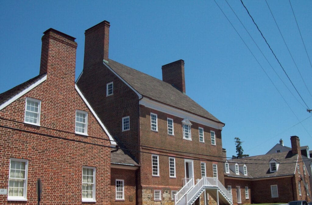 A 5-part brick mansion with three chimneys, and rows of windows overlooking a street