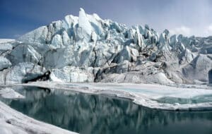 A large hill-shaped glacier rests above a clear pool of water reflecting the ice above